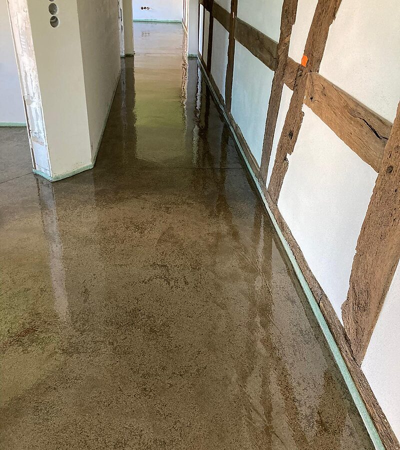 Sichtestrich im Umbau – heller fugenloser Zementestrich mit rustikalen Holzstützen in Altbau