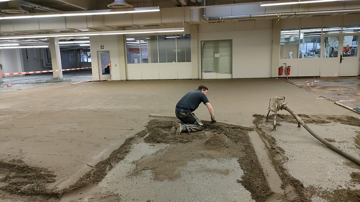 Schnellestrich Verlegung – Mitarbeiter legt Verbundzementestrich in großer Gewerbehalle maschinell mit Pumpe