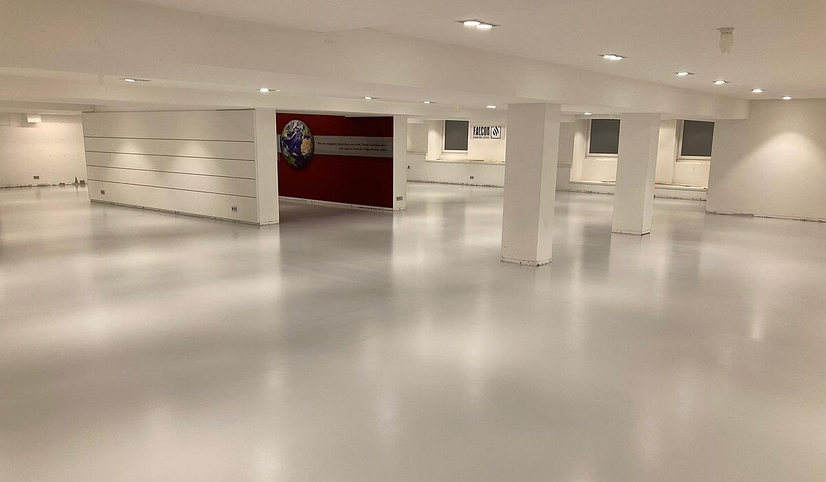 Weitläufiger Gewerberaum mit mattem hellgrauem Epoxidharz-Boden – gleichmäßige Bodenfläche mit weißen Säulen und Deckenleuchten