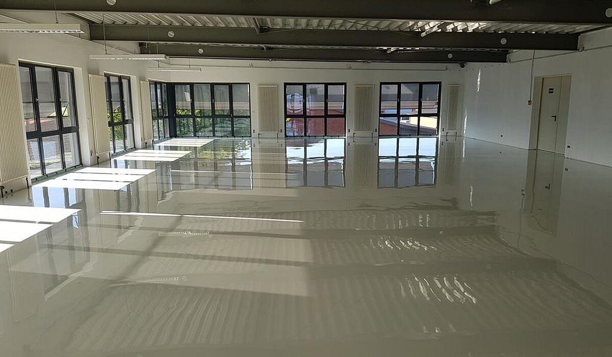 Hochglänzender Epoxidharz-Boden in Büro oder Gewerbehalle – Fensterfronten spiegeln sich im frisch verlegten Boden