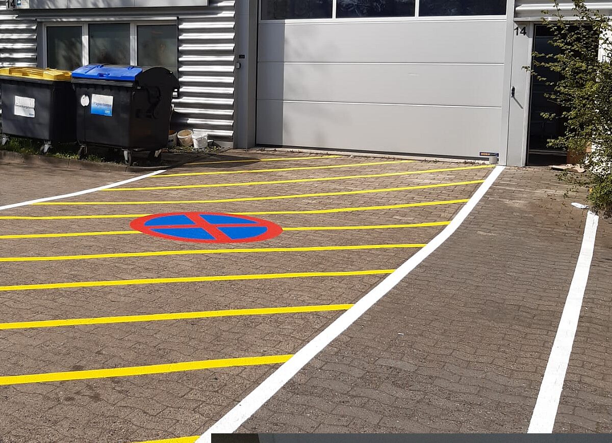 Außenparkplatz mit gelben Stellplatzlinien und aufgemaltem Halteverbotszeichen auf Pflasterboden – Zufahrt zu Gewerbehalle Nr. 14