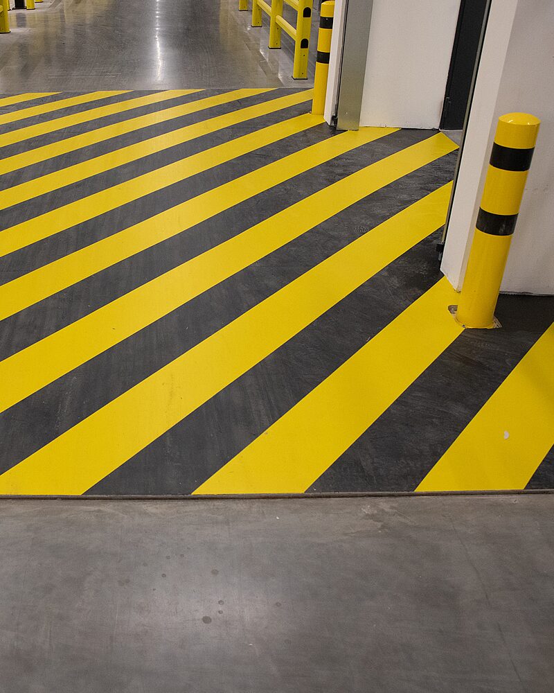 Gelb-schwarze diagonale Warnmarkierung an Tor-Durchgang in Lagerhalle – Sicherheitsmarkierung mit gelbem Rammschutzpfosten