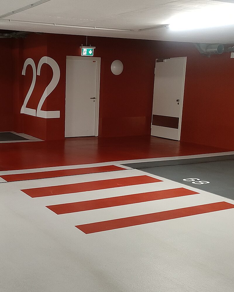 Tiefgaragenabschnitt mit rotem Fußgängerüberweg auf hellgrauem Boden und roter Wandgestaltung mit Etagennummer 22