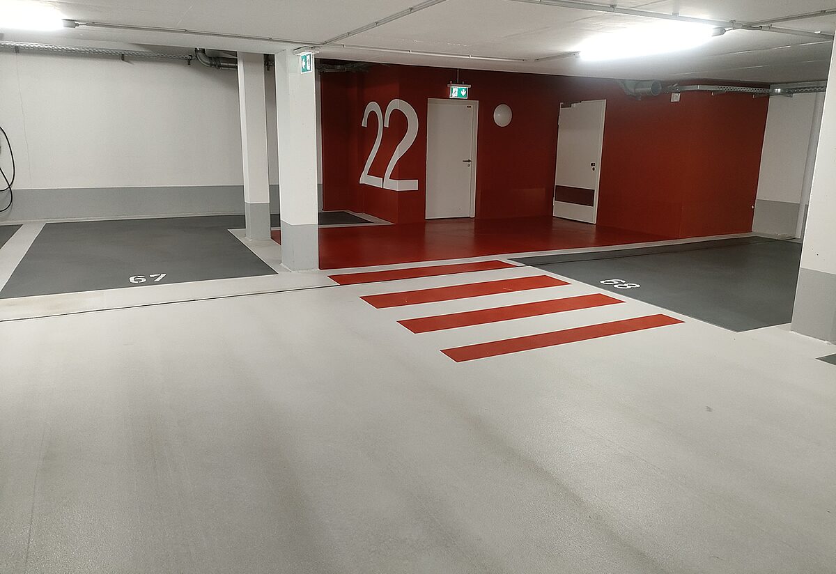 Tiefgarage mit zweifarbigem OS-8-Boden – schwarz-rote Wandgestaltung an Säulen, weiße Stellplatzlinien auf hellgrauem Boden