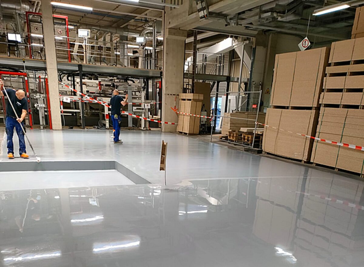 Drei Handwerker tragen Epoxidharz-Beschichtung auf einen Industrieboden in einer Lagerhalle auf