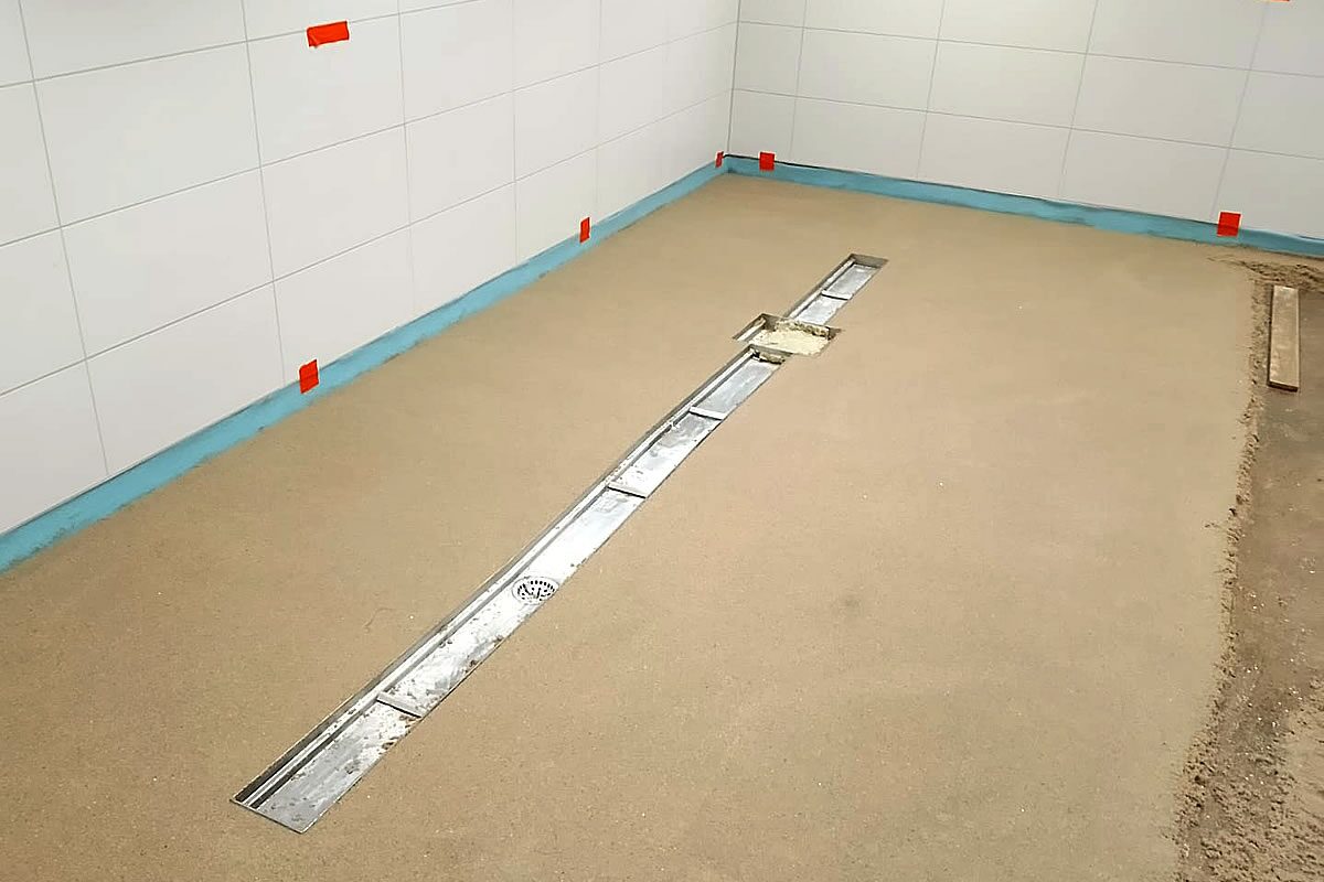 Industrieestrich mit eingelassener Edelstahlrinne und Bodenablauf vor gefliester Wand