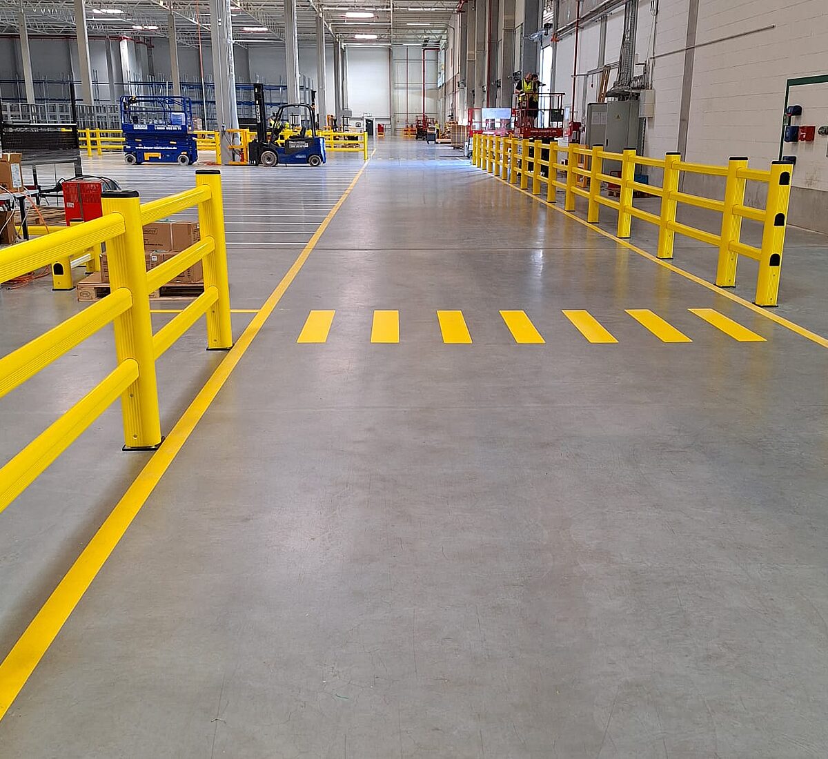 Industriehalle mit beschichtetem Betonboden, gelber Bodenmarkierung und gelben Rammschutz-Geländern