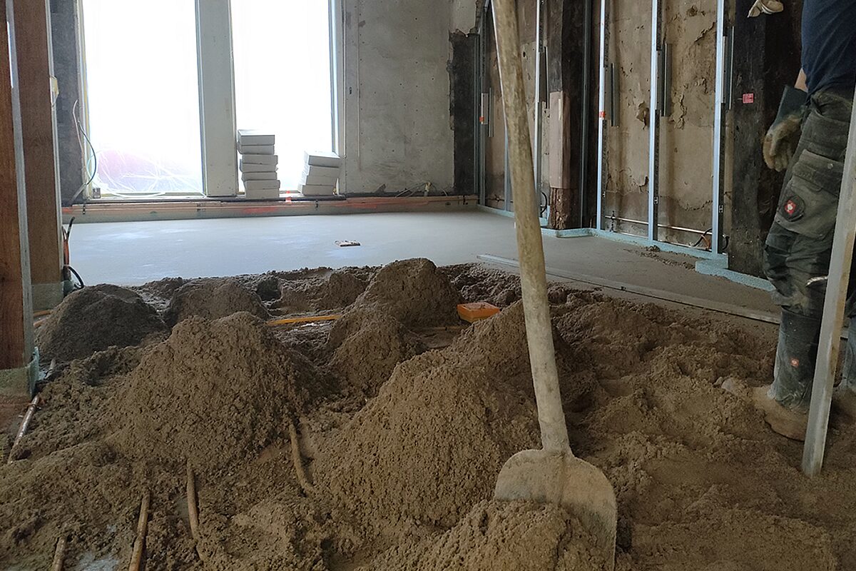 Estrichverlegung im Altbau Höxter – Vordergrund mit aufgehäuftem Estrichmaterial und Schaufel, Hintergrund frisch eingebrachte Estrichfläche an originalen Bestandswänden mit Stützprofilen