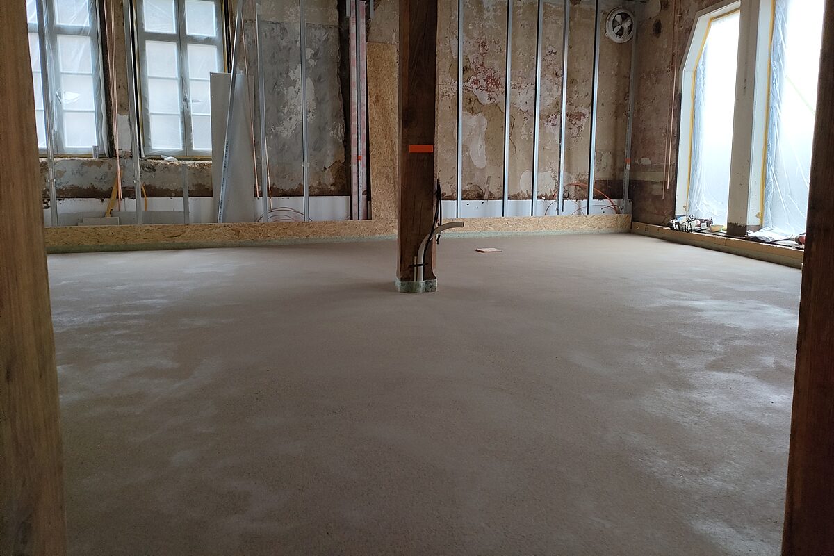 Großer Raum im Altbau Höxter nach Estrichverlegung – glatte fertige Estrichfläche, historische Fachwerkstütze in der Raummitte, originale Bestandswände und Fenster im Hintergrund