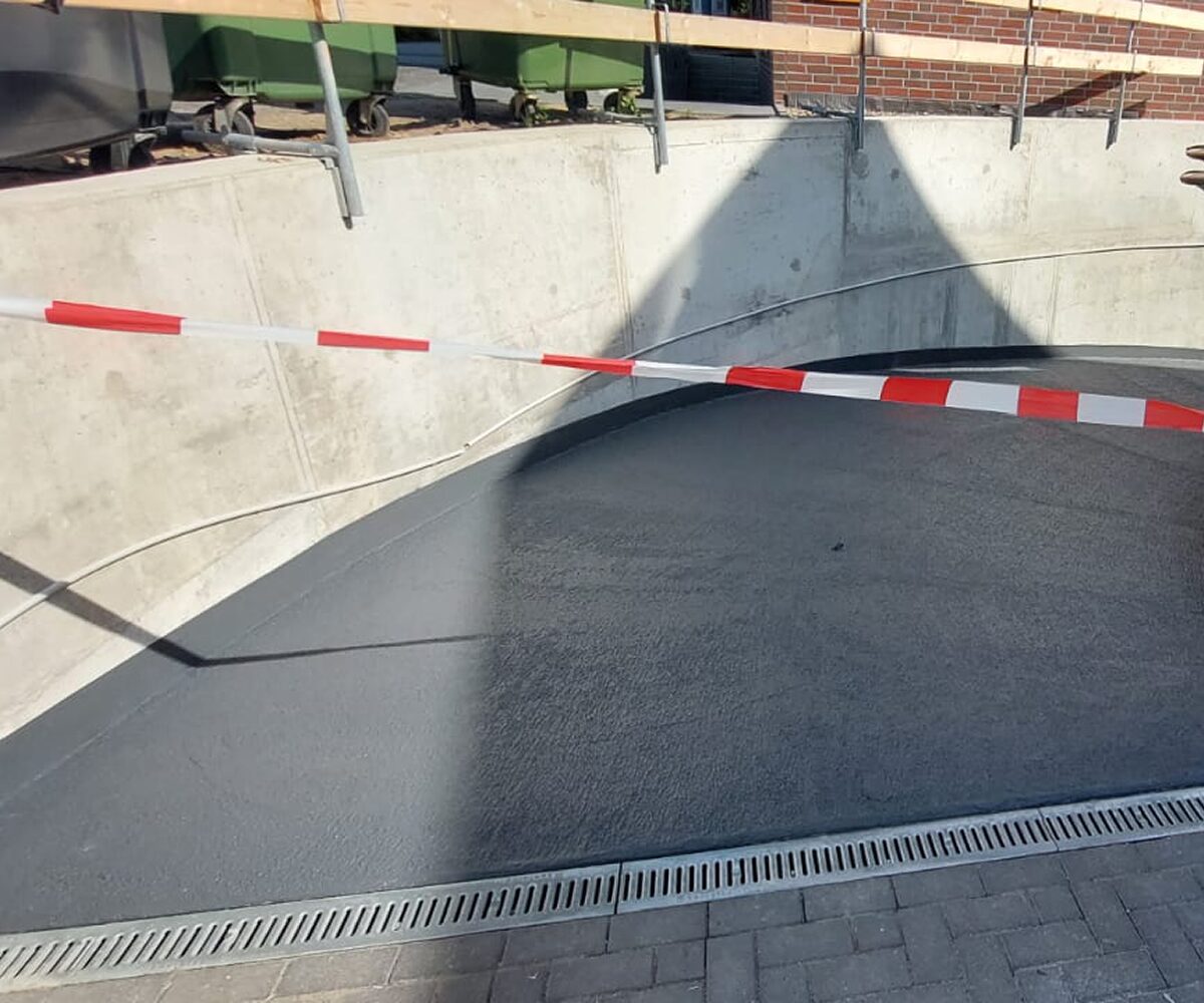 Fertig beschichtete Tiefgaragen-Rampe in Hannover mit anthrazitfarbener PMMA-Deckschicht und Entwässerungsrinne – abgesperrt bis zur vollständigen Aushärtung