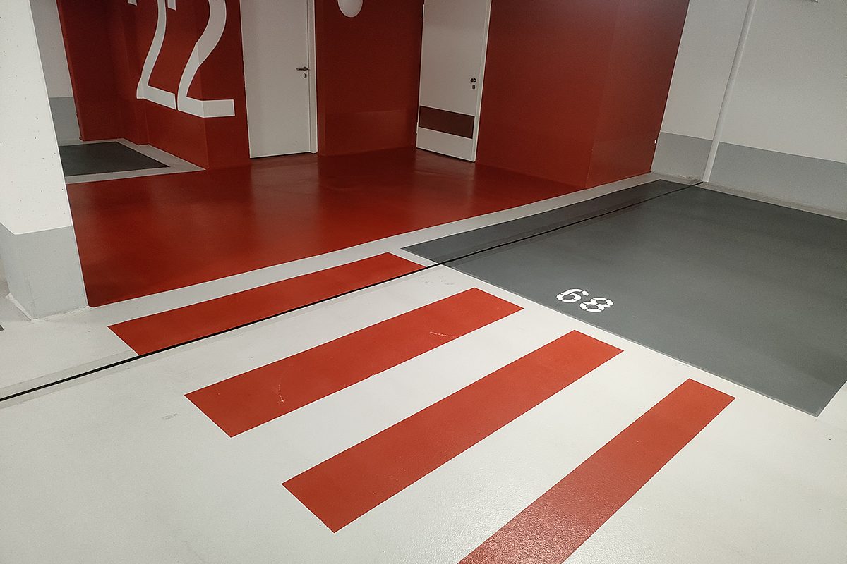OS 8 Beschichtung Detail – zwei Stellplätze 65 und 67 mit anthrazitfarbener Bodenfläche und weißer Trennstrichmarkierung, signalrote Wand mit Etagennummer 20 und Wallbox