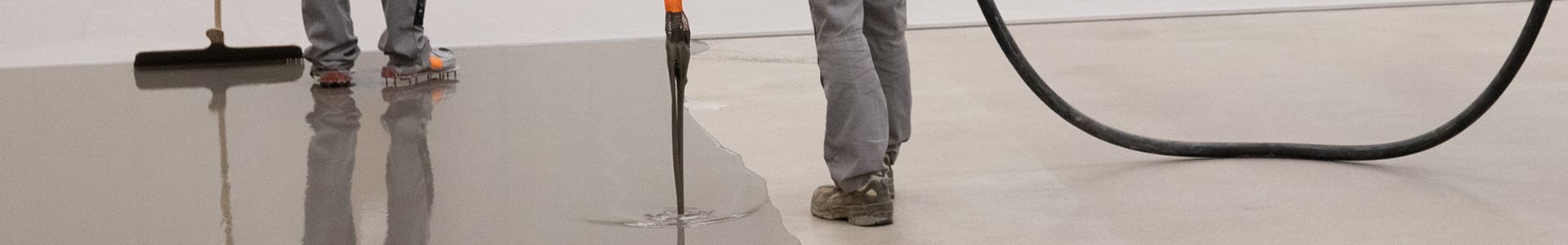 Aktuelle Baustelle – Kreie Industriebodenbeschichtung: zwei Mitarbeiter beim Auftragen von Fließestrich in einer Industriehalle