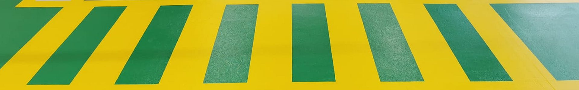 Dekorative Industriebodenbeschichtung – mehrfarbige Epoxidharz-Beschichtung mit gelb-grüner Sicherheitsmarkierung und schwarzem Fahrstreifen