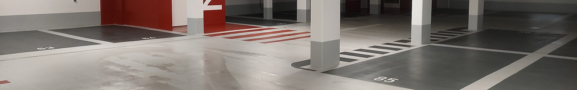 Industrieböden Beschichtung – Tiefgarage mit OS-8-Bodenbeschichtung, nummerierten Stellplätzen und roter Wandgestaltung
