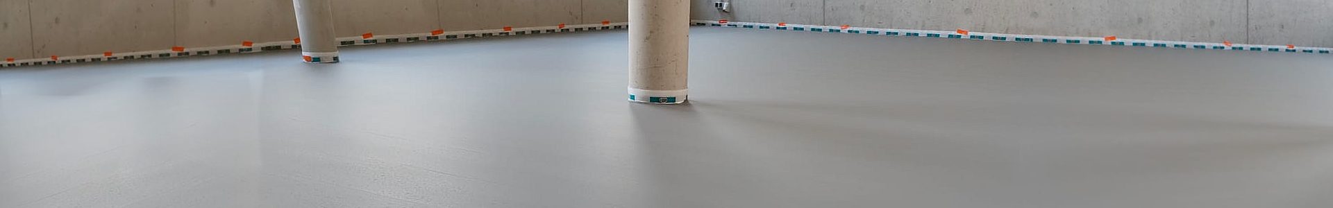 Zementfließestrich im Industriebau – frisch verlegter glatter Industrieboden mit Randstreifen und Stütze