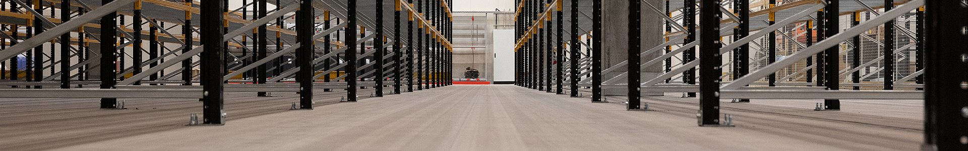 Industrieestrich im Hochregallager – glatter Betonboden zwischen schwarzen Stahlregalen in einer Industriehalle