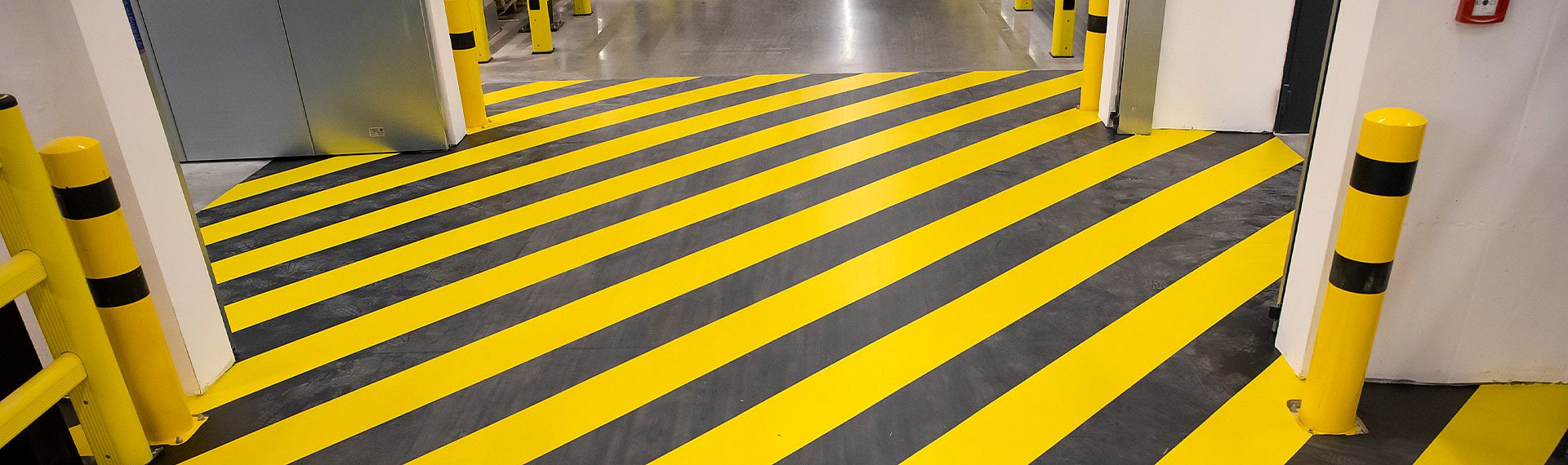 Industrieboden mit gelb-schwarzer Warnmarkierung und Rammschutzpfosten in einer Logistik- und Produktionshalle