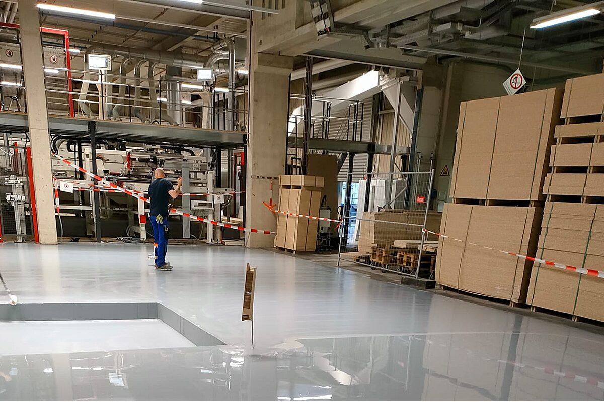 Handwerker trägt frische Industrieboden-Beschichtung in einer Produktionshalle auf – glänzende Epoxidharz-Oberfläche
