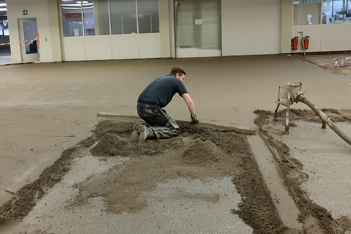 Handwerker pumpt Fließestrich auf Fußbodenheizungsmatte im Dachgeschoss – Estrichverlegung über Noppenmatte mit Dämmung und Heizschlangen