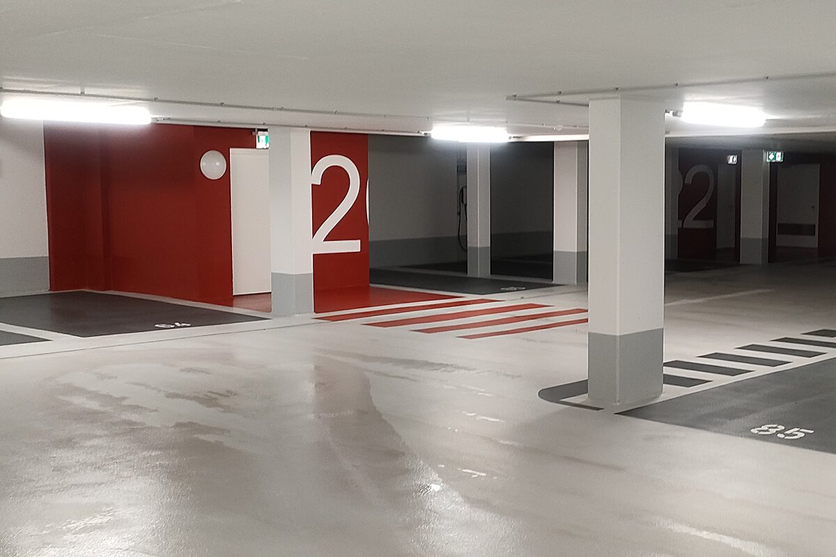 Tiefgarage mit professioneller Industrieboden-Beschichtung – mehrfarbige OS-8-Beschichtung mit roten Wandakzenten, Fußgängerüberwegen und nummerierten Stellplätzen