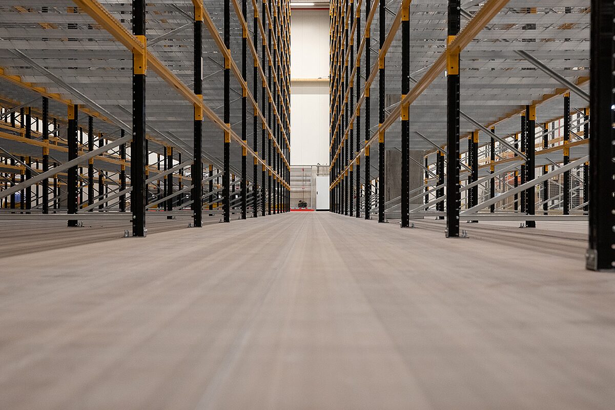 Hochregallager mit ebenem Industrieestrich – glatter maßgenauer Betonboden zwischen schwarz-gelben Hochregalreihen in großer Lagerhalle