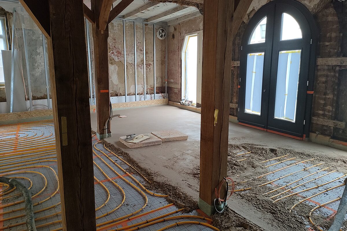 Denkmalgeschützter Altbau in Höxter bei der Sanierung – Estrichverlegung über Fußbodenheizungsrohren in historischem Gebäude mit Fachwerkstützen und Rundbogenfenstern