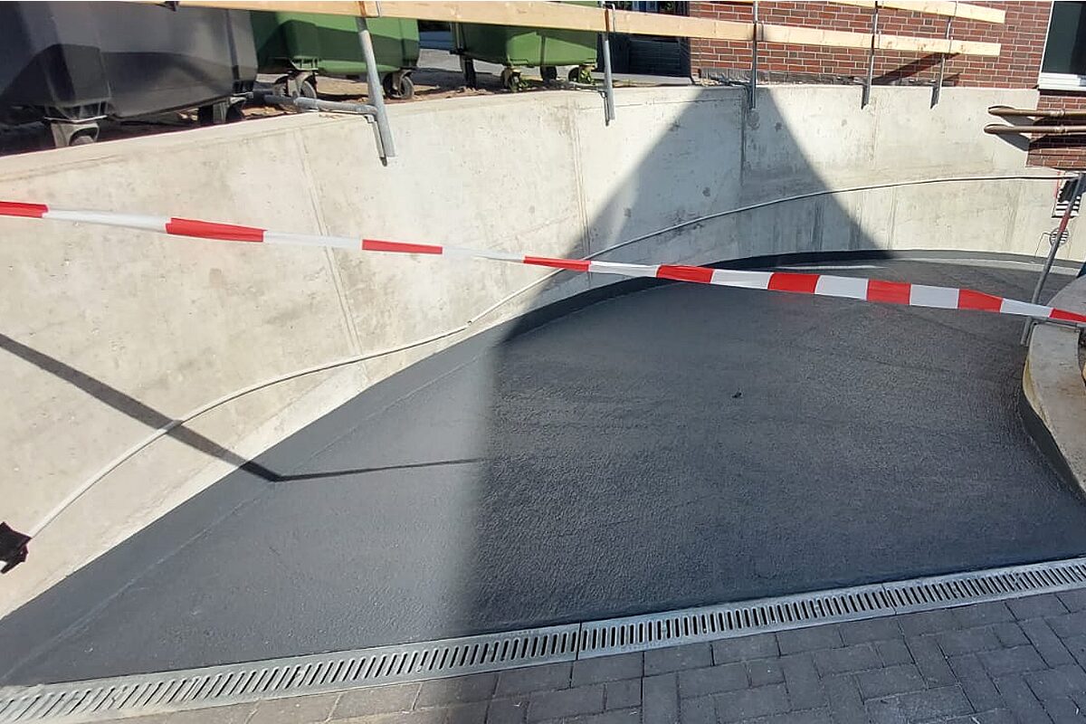Frisch beschichtete Tiefgaragenabfahrt in Hannover – anthrazitfarbene PMMA-Außenbeschichtung auf geschwungener Betonrampe mit Absperrband