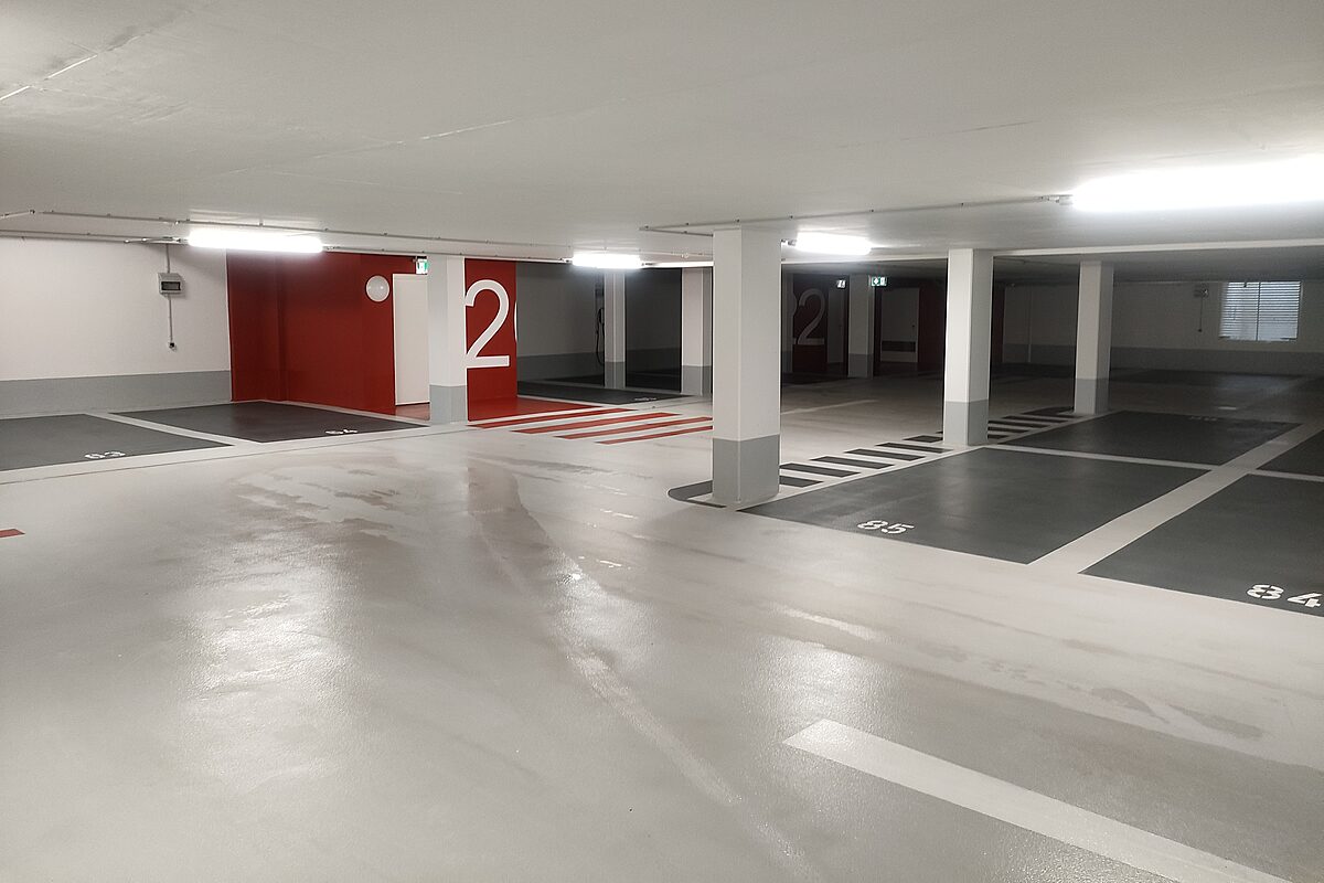 Tiefgarage in Hannover mit OS-8-Bodenbeschichtung – mehrfarbige Stellplätze, rote Wandgestaltung mit Etagennummern und Fußgängerüberwege